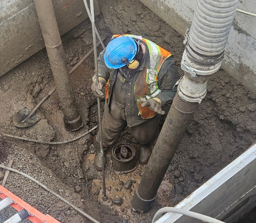 Crew member using a vacuum hose during hydro excavation in a trench