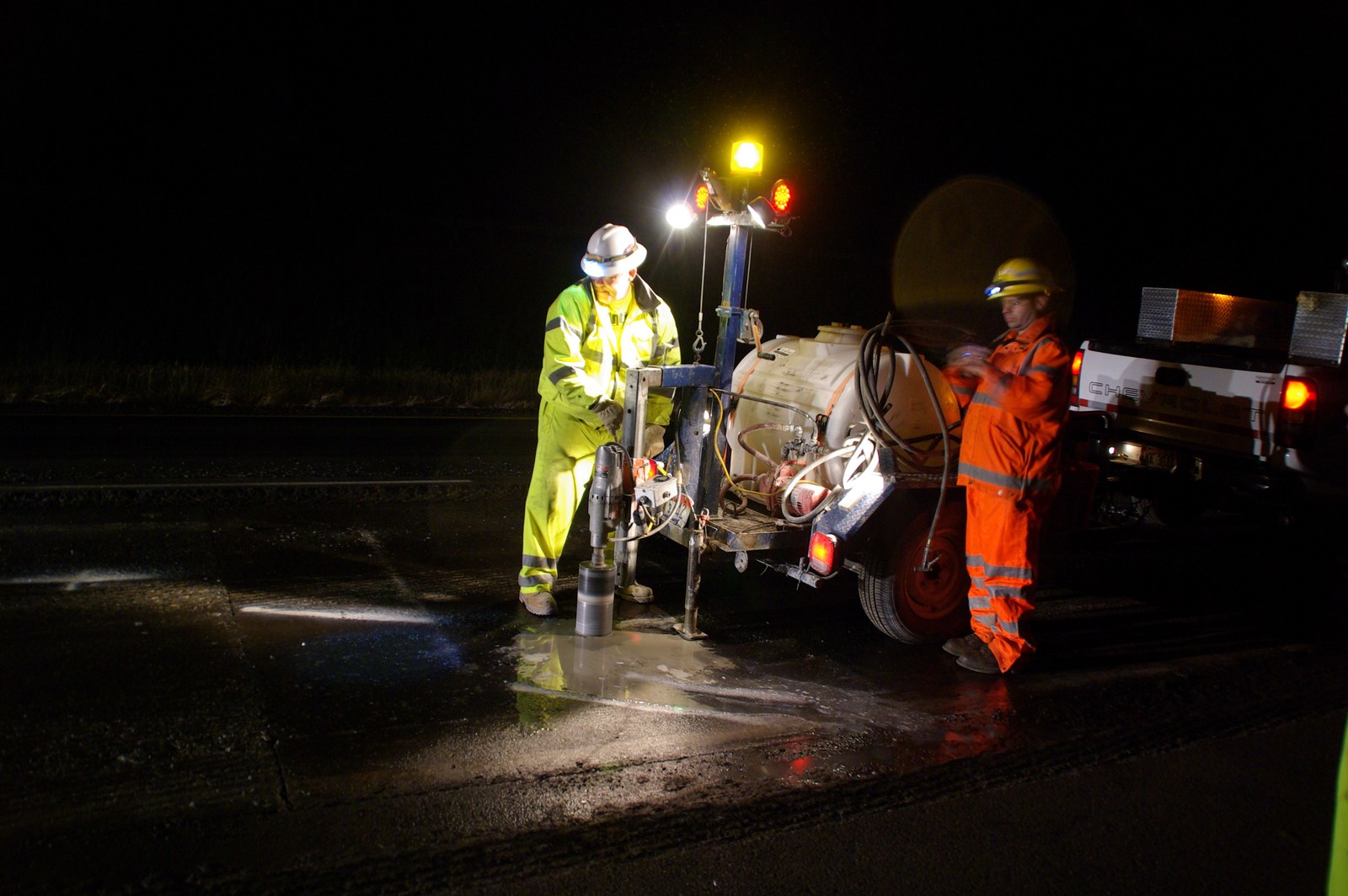 Core drilling rig cutting into pavement at a night job site with crew in high-visibility PPE
